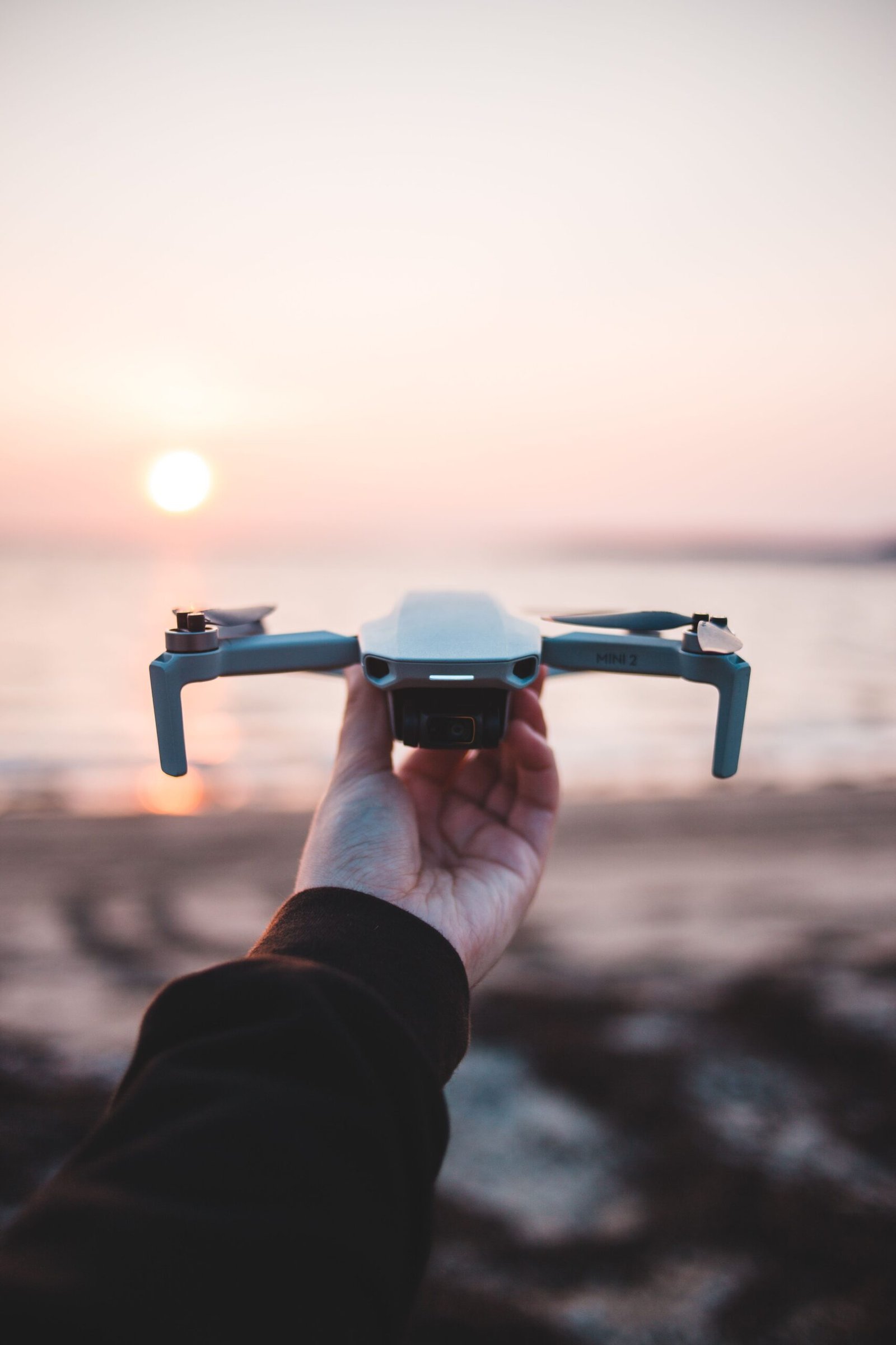 Close-up of a hand holding a drone at the beach during sunset.